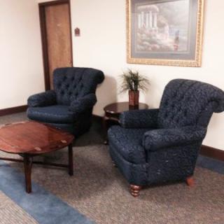 A cozy seating arrangement in a waiting area featuring two blue upholstered chairs and a wooden coffee table.
