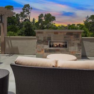 A cozy outdoor patio with a fireplace and seating, set against a sunset backdrop.