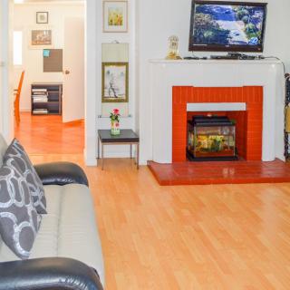 A cozy living room featuring a sofa, a television above an orange fireplace, and wooden flooring.