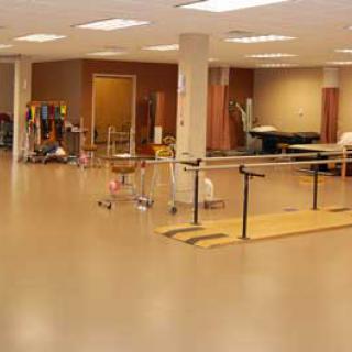 An interior view of a rehabilitation space equipped for physical therapy, featuring exercise bars and open floor space.