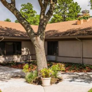 A small house with a sloped roof surrounded by a garden and a large tree in the courtyard.