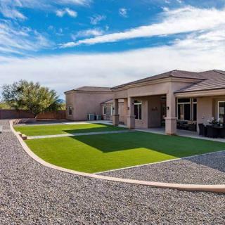 A sunny backyard featuring artificial grass and gravel landscaping around a modern house.
