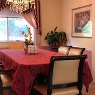 A dining room featuring a table with a red tablecloth, surrounded by chairs, decorated with a chandelier and curtains.