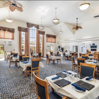 A spacious dining area with neatly arranged tables and chairs, featuring large windows and ceiling fans.