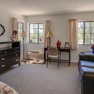 A cozy bedroom featuring a desk, chair, dresser, and windows with curtains.