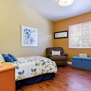 A cozy bedroom featuring a single bed with floral bedding, an armchair, and bright natural light.