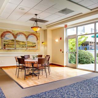 A well-lit dining area with a table and chairs, featuring artwork on the wall and large windows.