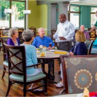 A group of seniors enjoying a meal together in a restaurant setting with attentive waitstaff.