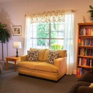 A cozy living room with a sofa, bookshelf, and large window letting in natural light.