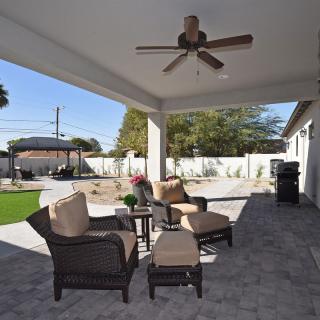 A cozy covered patio with comfortable outdoor seating and a ceiling fan, overlooking a landscaped backyard.