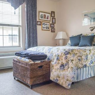 A cozy bedroom featuring a floral bedspread, decorative pillows, and a wicker basket at the foot of the bed.