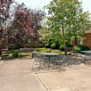 A serene outdoor courtyard featuring tables and benches surrounded by lush greenery.