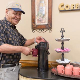 A cheerful elderly man serving coffee in a cozy kitchen setting.