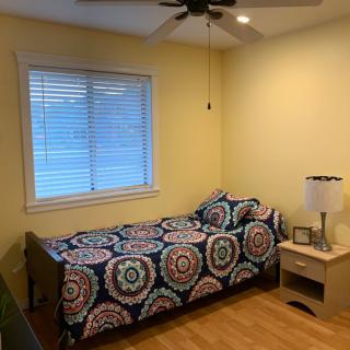 A cozy bedroom with a single bed featuring colorful bedding, a nightstand with a lamp, and a window illuminating the room.