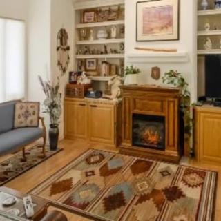 A cozy living room with a fireplace, patterned carpet, and decorative shelves.