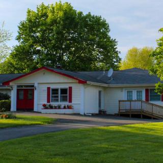 A single-story house with a red door and shutters, surrounded by trees and a well-maintained lawn.