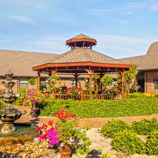 A beautiful garden featuring a wooden gazebo surrounded by vibrant flowers and a fountain.