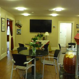 A modern waiting area featuring a large television, round glass tables, and chairs with plants for decoration.