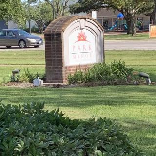 A park sign surrounded by greenery and a nearby road with a car.