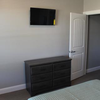 A minimalist bedroom with a wall-mounted TV and a dark dresser.