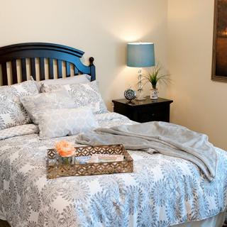 A cozy bedroom with patterned bedding and a bedside lamp.