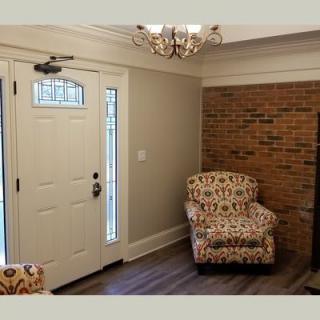 A cozy home entrance with a patterned armchair next to the door, featuring a brick accent wall and chandelier.