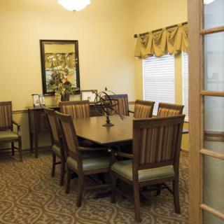 A neatly arranged dining room with a wooden table and chairs, featuring a mirror and window with drapes.