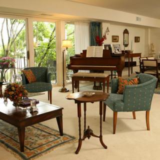 A cozy living room with elegant furniture, featuring a piano and large windows allowing natural light to fill the space.