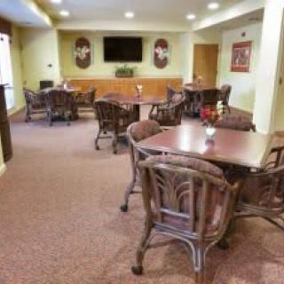 A cozy dining area with several tables and chairs, a TV mounted on the wall, and soft carpet flooring.