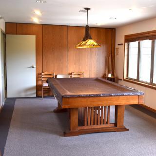 A well-lit room featuring a large wooden table and chairs, with natural light streaming through the windows.
