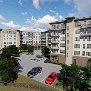 A modern apartment building with a parking lot and surrounding greenery under a partly cloudy sky.