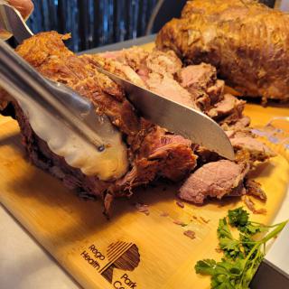 A chef carves a piece of roasted meat on a wooden cutting board.