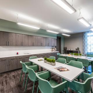 A modern office kitchen area featuring a large table with teal chairs and gray cabinetry.