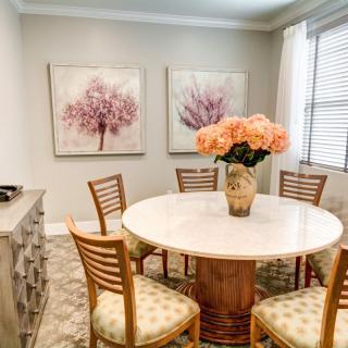A cozy dining room featuring a round table with a floral centerpiece and decorative wall art.
