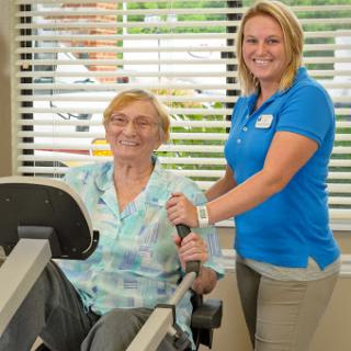 A personal trainer assists a senior client during a workout session in a rehabilitative fitness environment.