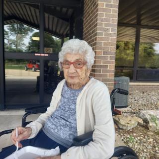 An elderly woman enjoying a sunny day outside in her wheelchair.