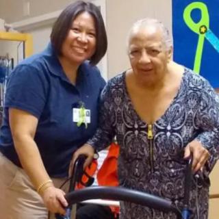 A healthcare worker assisting an elderly woman with a walker.