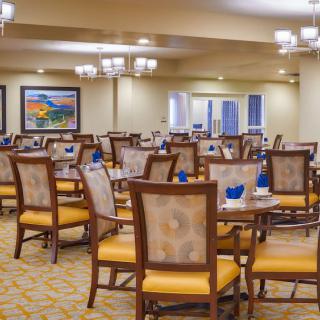 A spacious dining area with neatly arranged tables and chairs, featuring elegant chandeliers and modern decor.