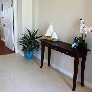 A welcoming entryway features a dark wooden console table adorned with a sailboat model, orchid, and picture frame, alongside a vibrant potted plant.