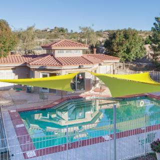 A backyard with a swimming pool featuring shade sails and a fenced area.