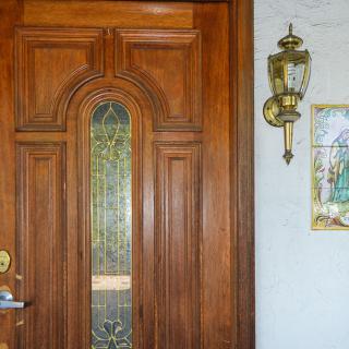 A wooden front door with stained glass, accompanied by a wall-mounted lantern and decorative artwork.