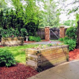 A beautifully landscaped garden with wooden planters, lush greenery, and a pathway leading to a wooden gate.
