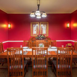 A formal dining room with wooden furniture and red walls, featuring a chandelier and decorative lighting.