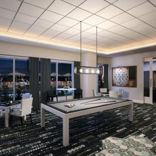 A modern living space with a pool table, contemporary furniture, and large windows providing ample natural light.