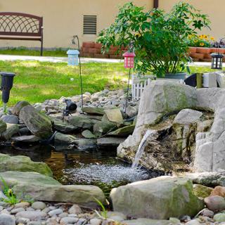 A tranquil garden pond with a small waterfall surrounded by rocks and greenery.