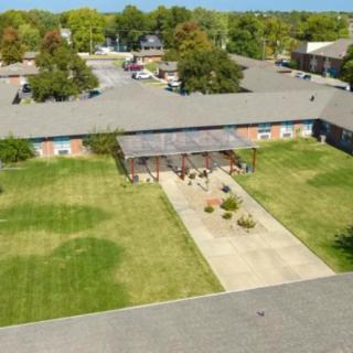 Aerial view of a single-story building with a central driveway, surrounded by grass and trees.