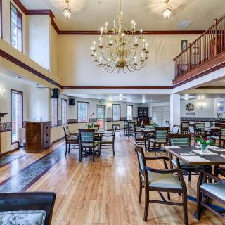 A spacious, well-lit dining area with elegant chandeliers and neatly arranged tables and chairs.