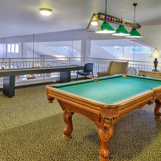 A spacious game room featuring a pool table under green-hued hanging lights.