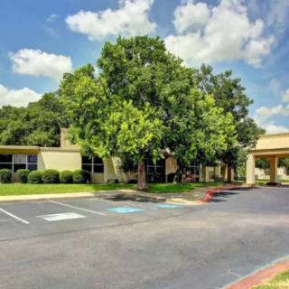 A sunny day view of a building surrounded by trees with an adjacent parking lot.