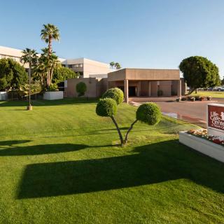A modern building surrounded by a well-maintained lawn and neatly trimmed trees on a sunny day.